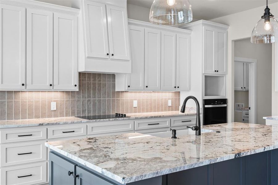 Kitchen featuring white cabinetry, an island with sink, light stone countertops, and pendant lighting