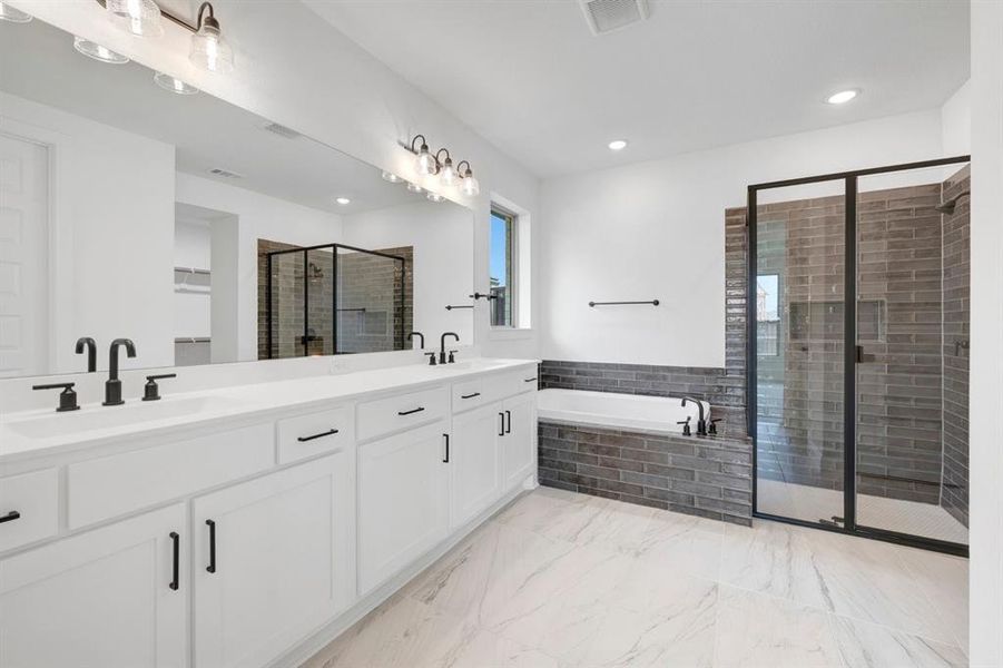 Spacious bathroom featuring a dual vanity with white cabinetry and quartz countertops, an undermount soaking tub, and a separate walk-in shower with dark brick-patterned tile and black-framed glass enclosure