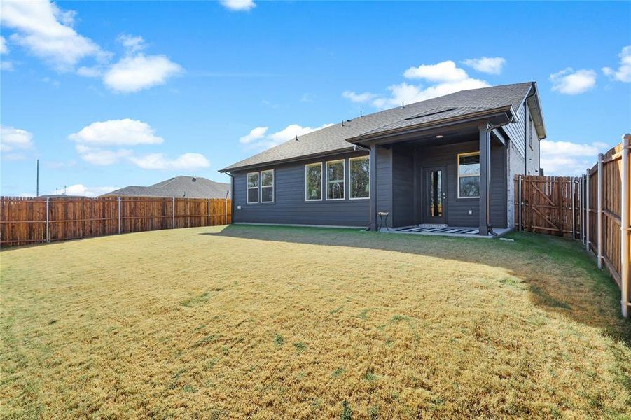 Expansive backyard featuring a privacy fence, covered patio with patterned tile, full-light glass door, and multiple large windows
