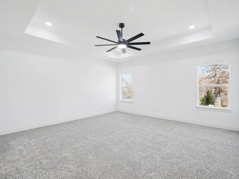 Unfurnished room with light carpet, ceiling fan, and a tray ceiling