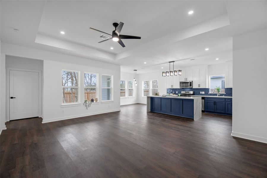 Spacious open-concept area with elegant dark hardwood floors leading into a modern kitchen. The room is bright and airy, thanks to ample windows and recessed lighting.
