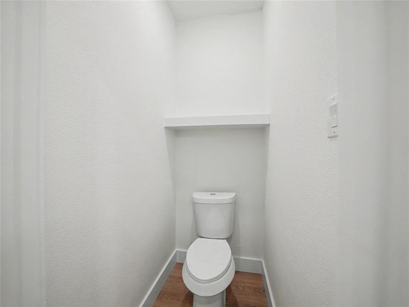 Recessed toilet alcove featuring a built-in white shelf, white baseboards, and wood-finish flooring Recessed toilet alcove featuring a built-in white shelf, white baseboards, and wood-finish flooring