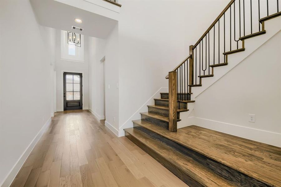 Entryway featuring a two-story ceiling, wood-finish flooring, a dark-paneled front door, and a staircase with wood treads and metal balusters Entryway featuring a two-story ceiling, wood-finish flooring, a dark-paneled front door, and a staircase with wood treads and metal balusters