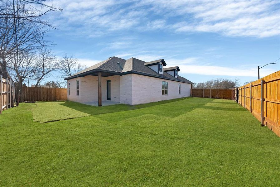 Back of property featuring brick siding, a fenced backyard, a patio area, and roof with shingles