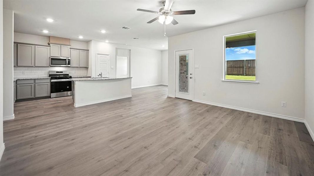 Open-concept living space featuring wood-finish flooring, a contemporary kitchen with stainless steel appliances, grey cabinetry, a white subway tile backsplash, and a breakfast bar