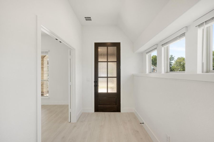 Empty room with white walls, light wood floors, and a dark wood glass-panel door