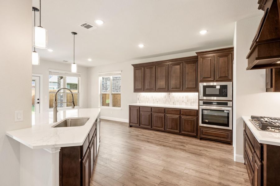 Kitchen with dark wood cabinets, white quartz countertops, stainless steel appliances, and light hardwood floors
