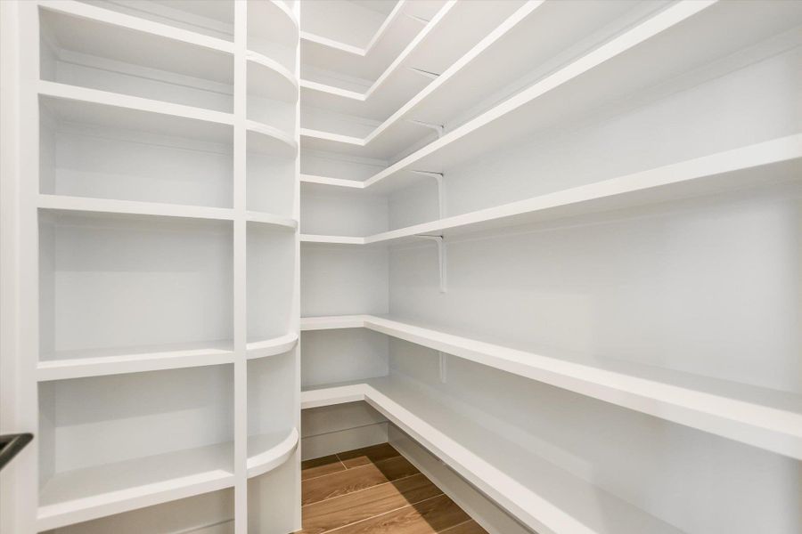 Expansive walk-in pantry featuring white shelving, a rounded shelving unit, and wood-finish flooring