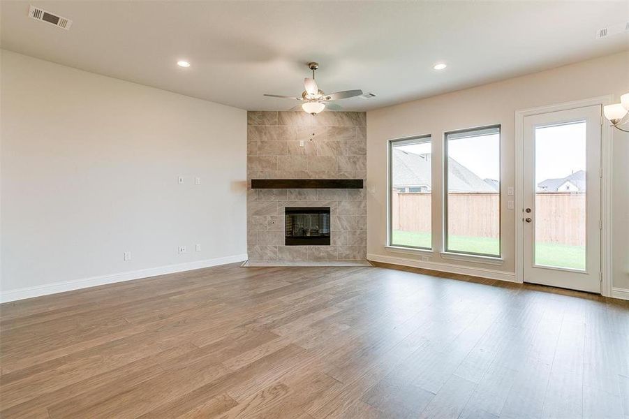 Unfurnished living room featuring a tiled fireplace, tile walls, light hardwood / wood-style flooring, and a healthy amount of sunlight