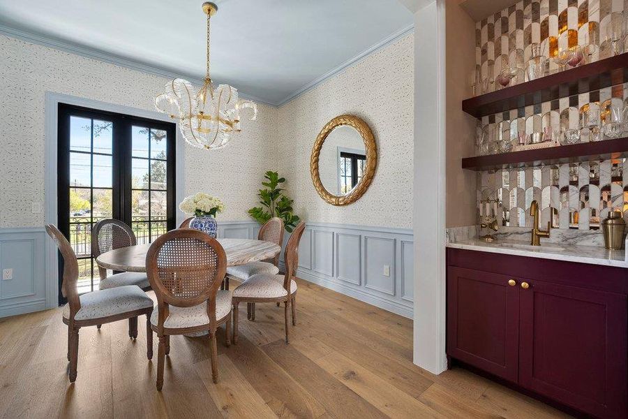 Dining area with light wood-style floors, a decorative wall, crown molding, suspended lighting, and wallpapered walls