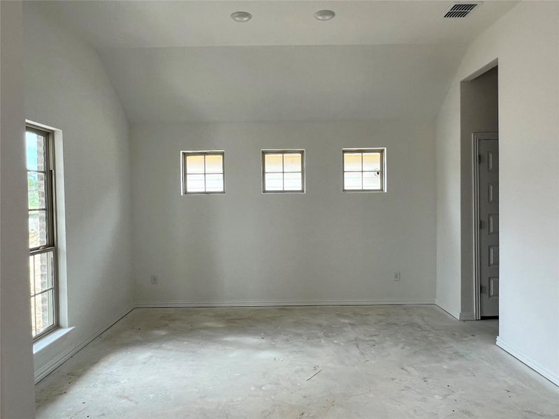 Unfurnished room featuring vaulted ceiling, plenty of natural light, and unfinished concrete flooring