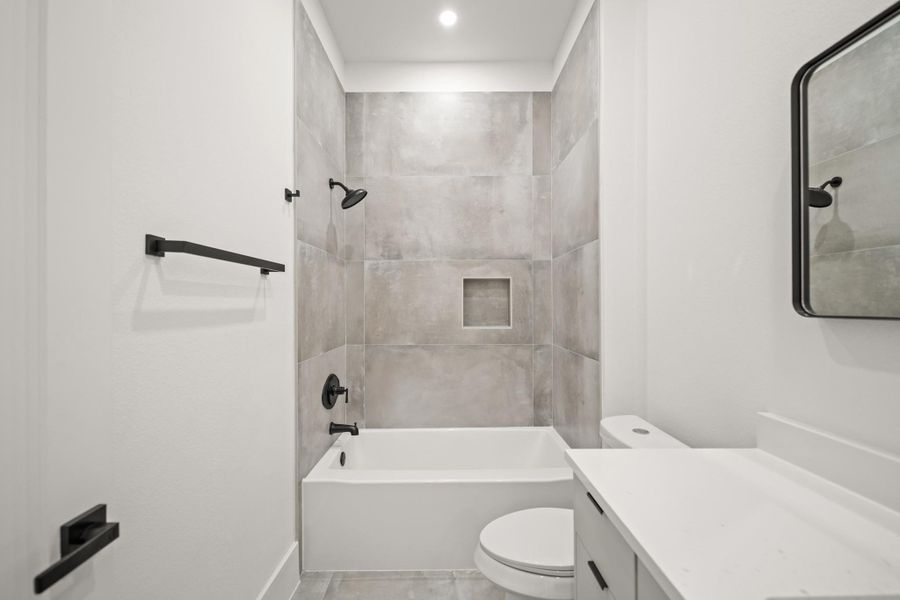 Another view of the ensuite bath with towel rod, vanity with quartz counter and large tile flooring, perfect for guests when retreating to the third bedroom on the first floor.