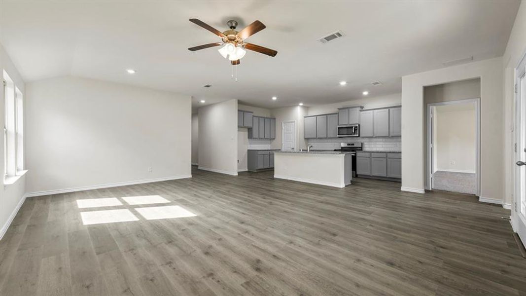 Open-concept living area with wood-finish flooring, vaulted ceilings, and a kitchen featuring gray cabinetry, a subway tile backsplash, and a central island