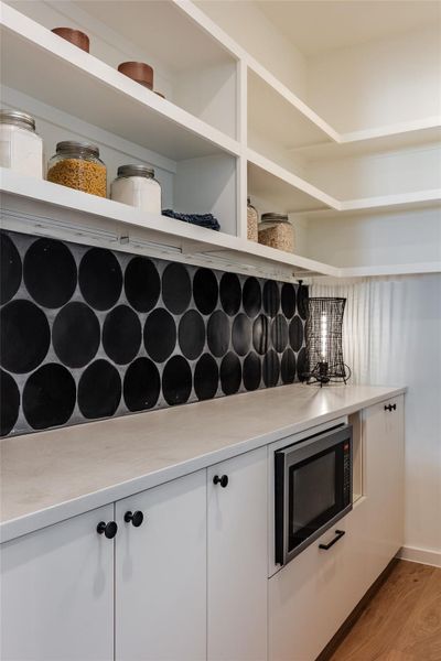 Kitchen featuring white cabinets, stainless steel microwave, backsplash, and light wood-type flooring