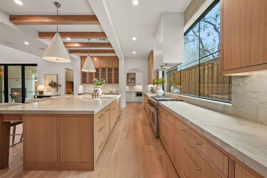 Kitchen with beamed ceiling, light stone counters, glass insert cabinets, a kitchen breakfast bar, and stainless steel appliances Kitchen with beamed ceiling, light stone counters, glass insert cabinets, a kitchen breakfast bar, and stainless steel appliances