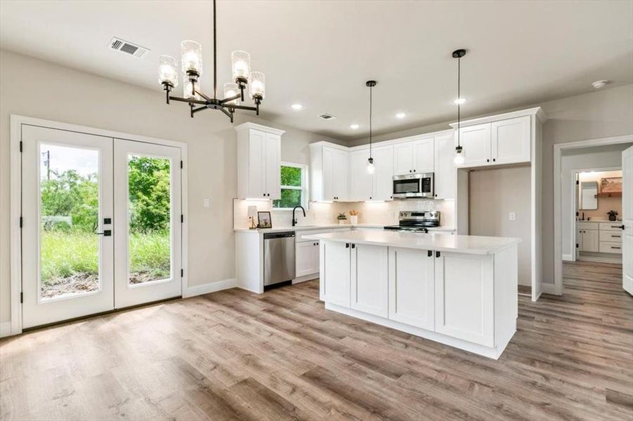 Modern kitchen featuring white shaker cabinetry, stainless steel appliances, a center island with pendant lighting, stone countertops, and wood-finish flooring