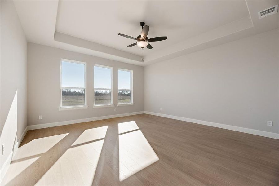 Empty room with a raised ceiling, light wood-type flooring, and ceiling fan Empty room with a raised ceiling, light wood-type flooring, and ceiling fan