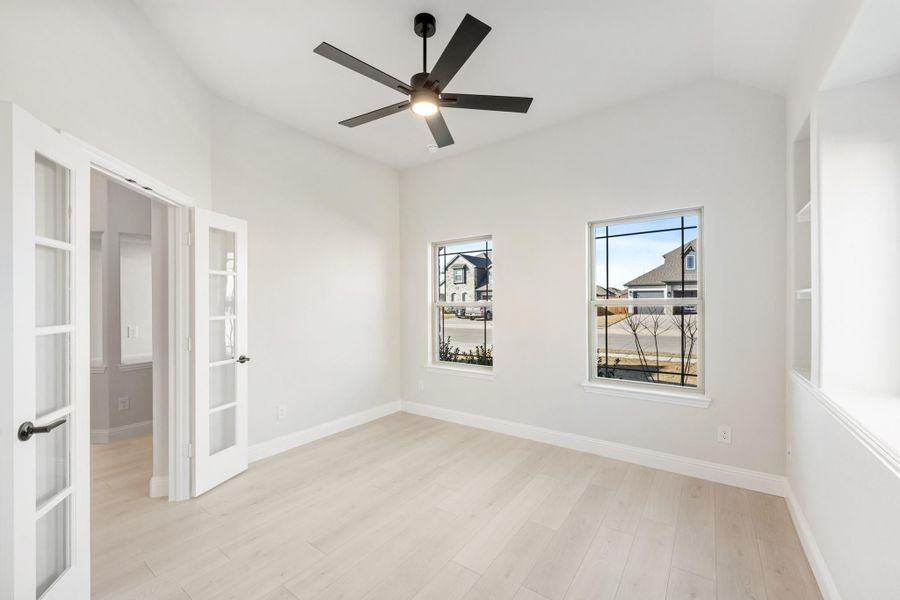 Empty room with light hardwood floors, black ceiling fan, and French doors with two windows