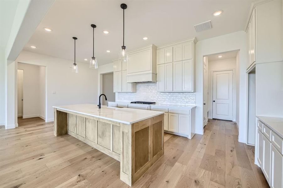 Kitchen featuring an island with sink, white cabinetry, custom range hood, and light hardwood / wood-style flooring