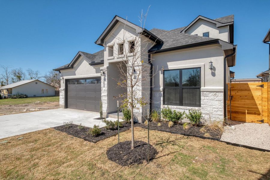 View of front facade featuring stucco siding, driveway, stone siding, roof with shingles, and an attached garage