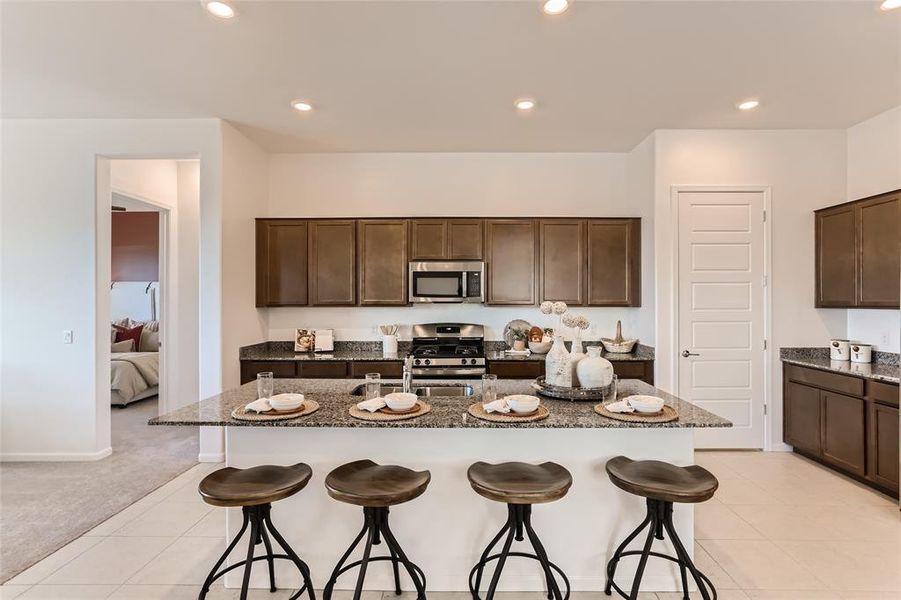 Kitchen featuring dark brown cabinetry, dark stone counters, recessed lighting, appliances with stainless steel finishes, and an island with sink