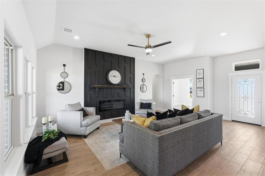 Living room featuring a large fireplace, light wood-type flooring, recessed lighting, ceiling fan, and arched walkways