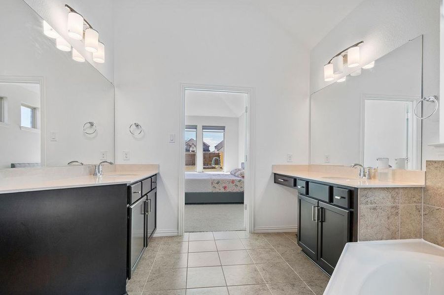 Ensuite bathroom with two vanities, light tile patterned flooring, a bath, and lofted ceiling Ensuite bathroom with two vanities, light tile patterned flooring, a bath, and lofted ceiling