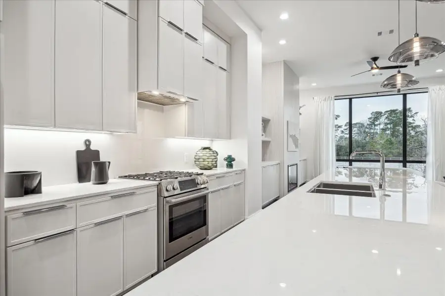 Chef-inspired kitchen appointed with Dekton Malibu countertops, an oversized waterfall island with seating, Bosch stainless steel appliances, gas cooktop, convection oven, custom cabinetry, under-cabinet lighting, and a spacious walk-in pantry. Pendant lighting and clean-lined finishes create a polished yet functional space ideal for entertaining and daily living in this Memorial residence.