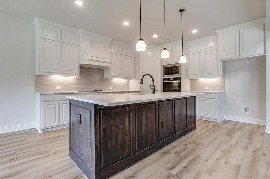 Kitchen with white cabinetry, premium range hood, black appliances, tasteful backsplash, and light hardwood / wood-style floors