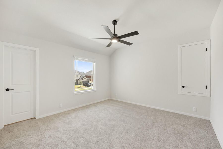 Empty bedroom with vaulted ceiling, ceiling fan, carpet flooring, and two white doors