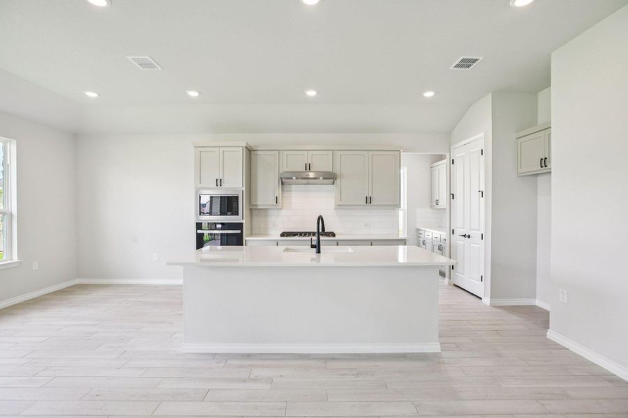 Kitchen with backsplash, recessed lighting, a center island with sink, black oven, and light stone counters