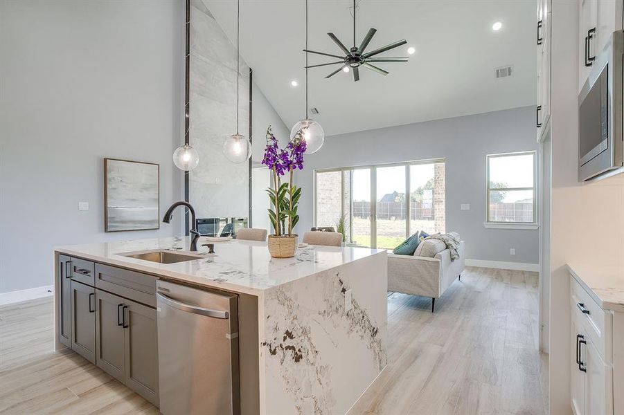 Kitchen with high vaulted ceiling, light stone counters, stainless steel appliances, light wood-style floors, and decorative light fixtures