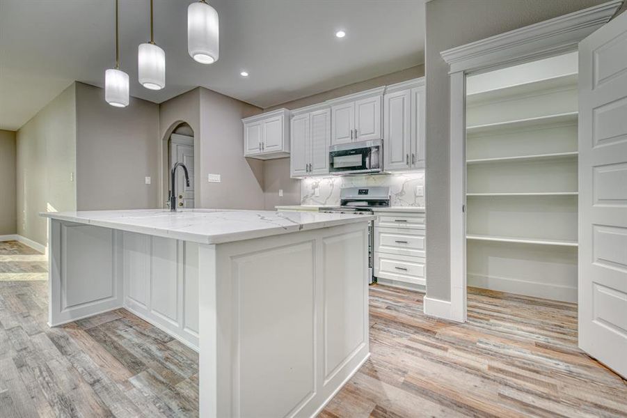 Kitchen featuring white cabinetry, arched walkways, light stone countertops, decorative light fixtures, and decorative backsplash