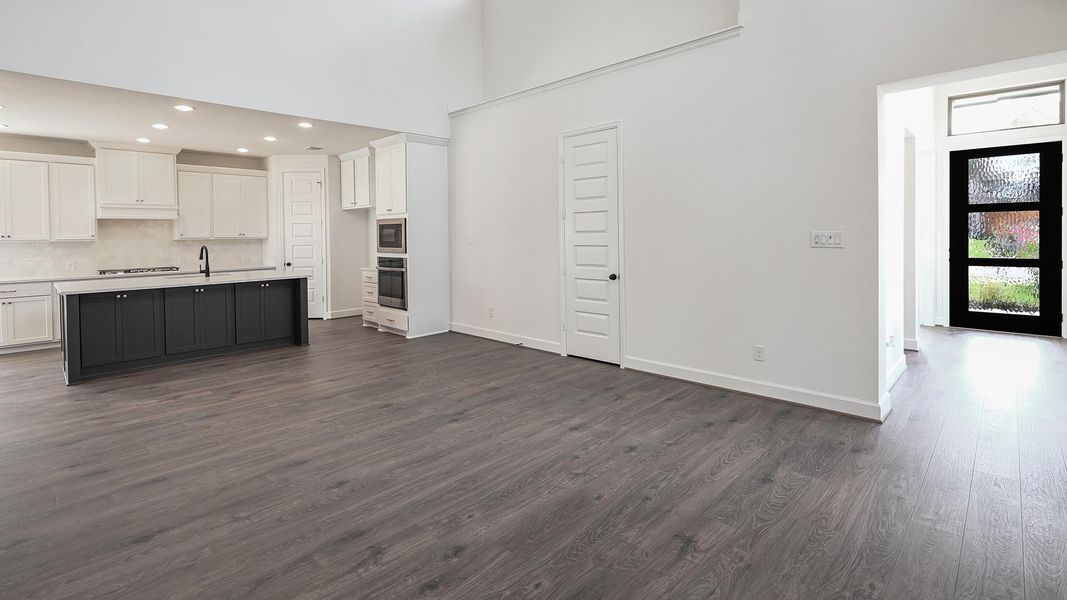 Kitchen with white cabinets, dark wood finished floors, a towering ceiling, backsplash, and an island with sink