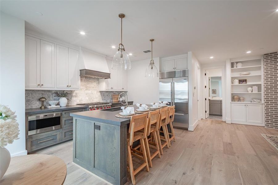 Kitchen with a kitchen island with sink, premium range hood, appliances with stainless steel finishes, light hardwood / wood-style floors, and white cabinetry