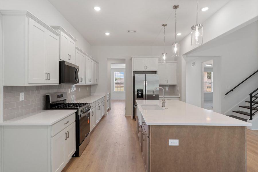 Kitchen featuring white shaker cabinetry, stainless steel appliances, light wood-finish flooring, a large island with an undermount sink, and pendant lighting Kitchen featuring white shaker cabinetry, stainless steel appliances, light wood-finish flooring, a large island with an undermount sink, and pendant lighting