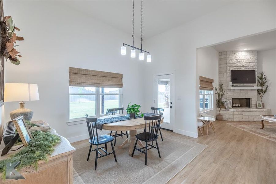 Dining space with light wood-style flooring, a stone fireplace, and a towering ceiling Dining space with light wood-style flooring, a stone fireplace, and a towering ceiling