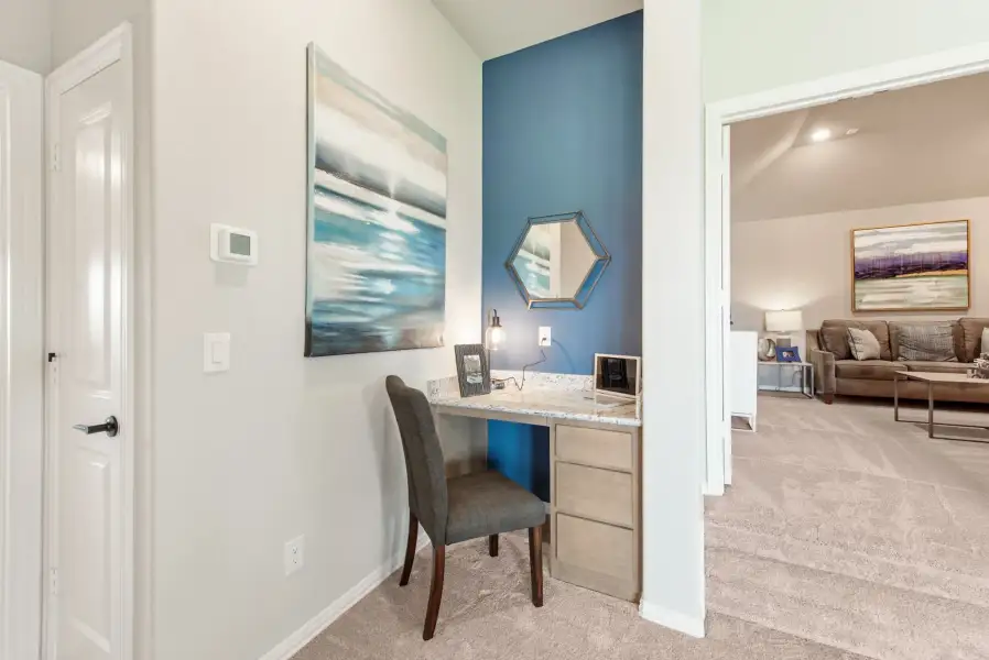Built-in desk nook with blue accent wall, stone countertop, and gray chair, with living room visible beyond