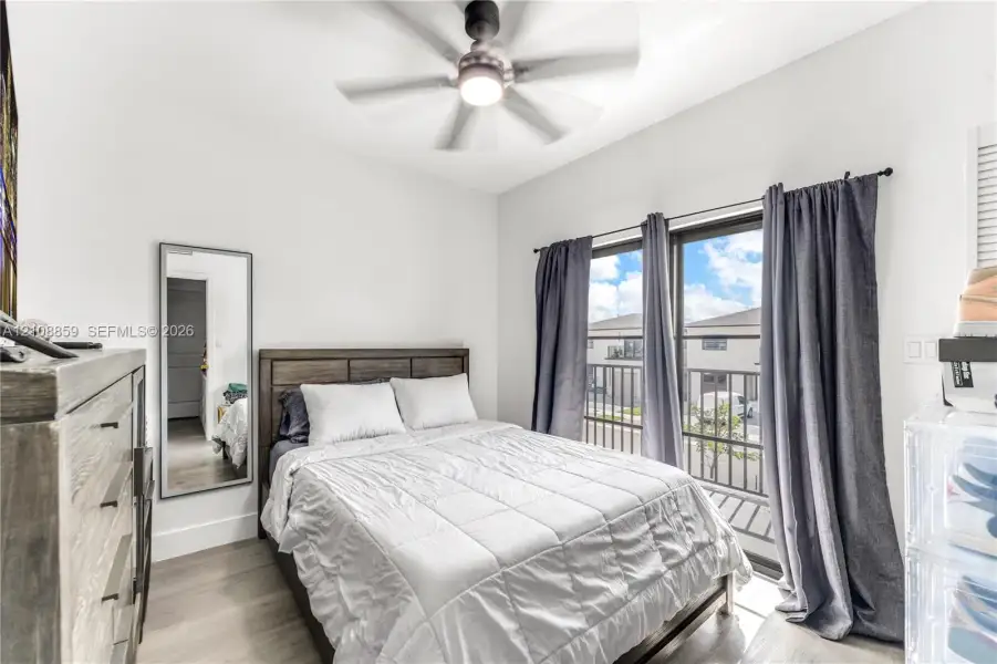 Room featuring wood-finish flooring, a ceiling fan with integrated lighting, and a sliding glass door providing access to a balcony with metal railing