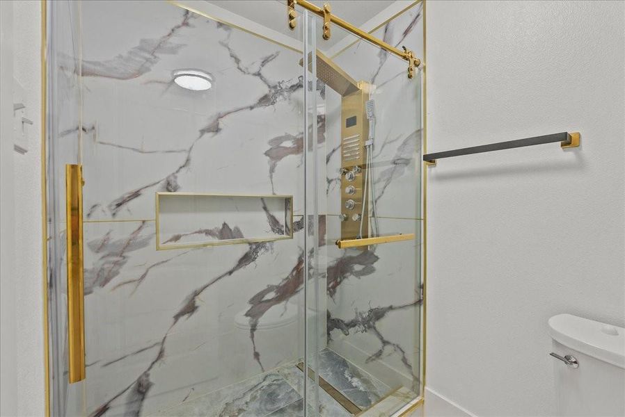 Spa-inspired walk-in shower with dramatic marble-look tile and gold accents.