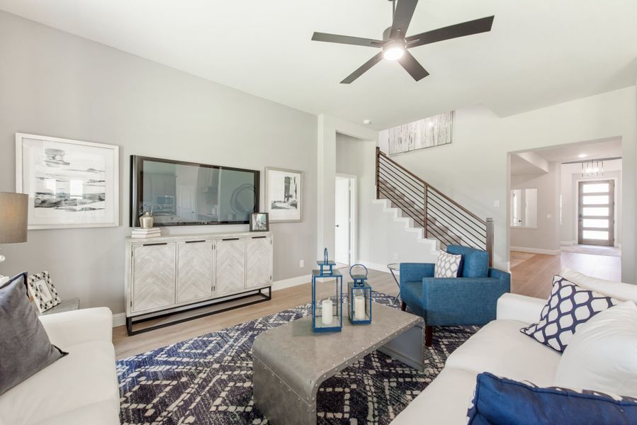 Living room with white sofa, blue accent chairs, large TV, and staircase with metal railing