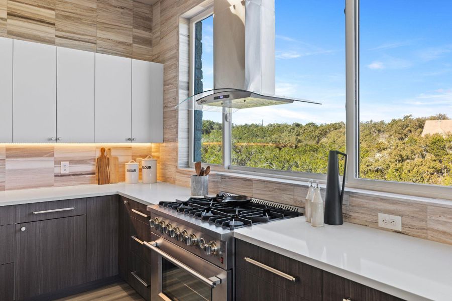 Kitchen featuring wall chimney range hood, dark brown cabinetry, light countertops, stainless steel stove, and white cabinets