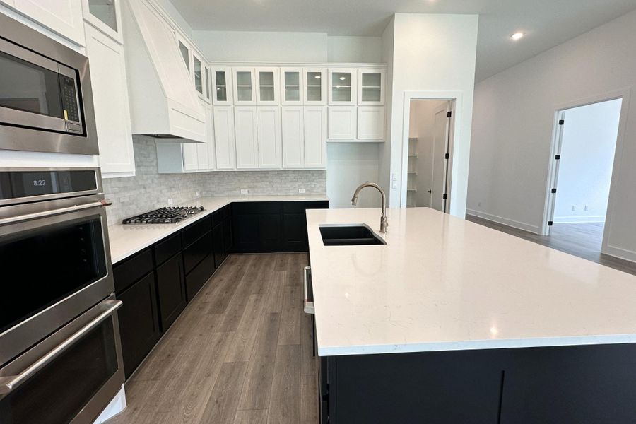 A well-lit kitchen with sleek dark cabinetry, stainless steel appliances, and a central island with a sink.