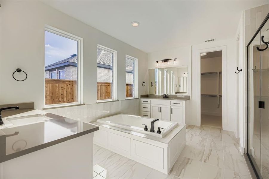Full bathroom with vanity, a garden tub, a spacious closet, a stall shower, and light marble finish flooring Full bathroom with vanity, a garden tub, a spacious closet, a stall shower, and light marble finish flooring