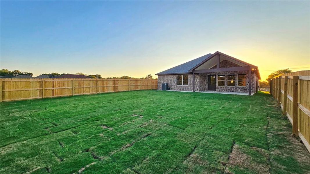 Back of house at dusk with a fenced backyard, a patio, and brick siding