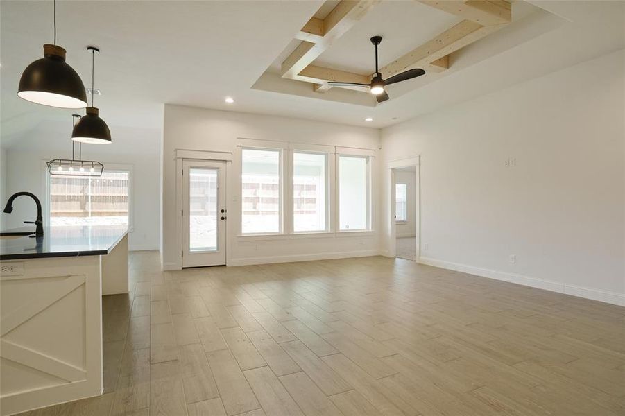 Unfurnished living room featuring ceiling fan, light wood-type flooring, sink, beam ceiling, and a raised ceiling