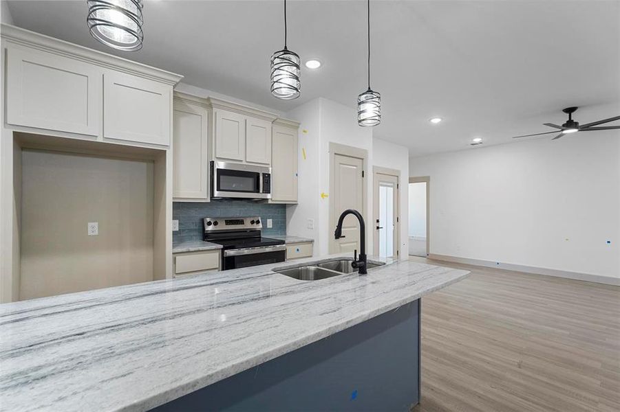 Kitchen featuring light stone countertops, light wood-style flooring, a sink, decorative backsplash, and stainless steel appliances