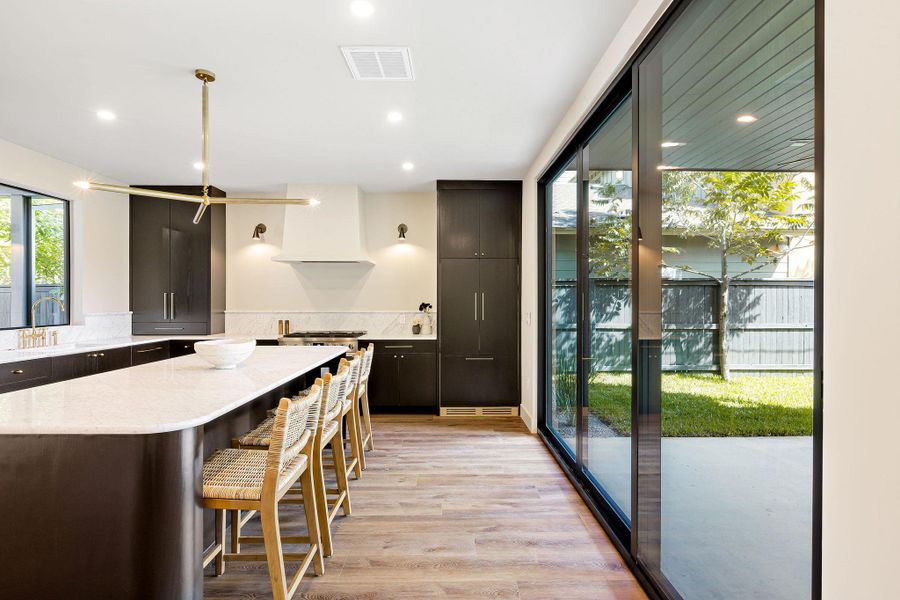 Kitchen with light wood-type flooring, light stone countertops, a kitchen breakfast bar, recessed lighting, and modern cabinets