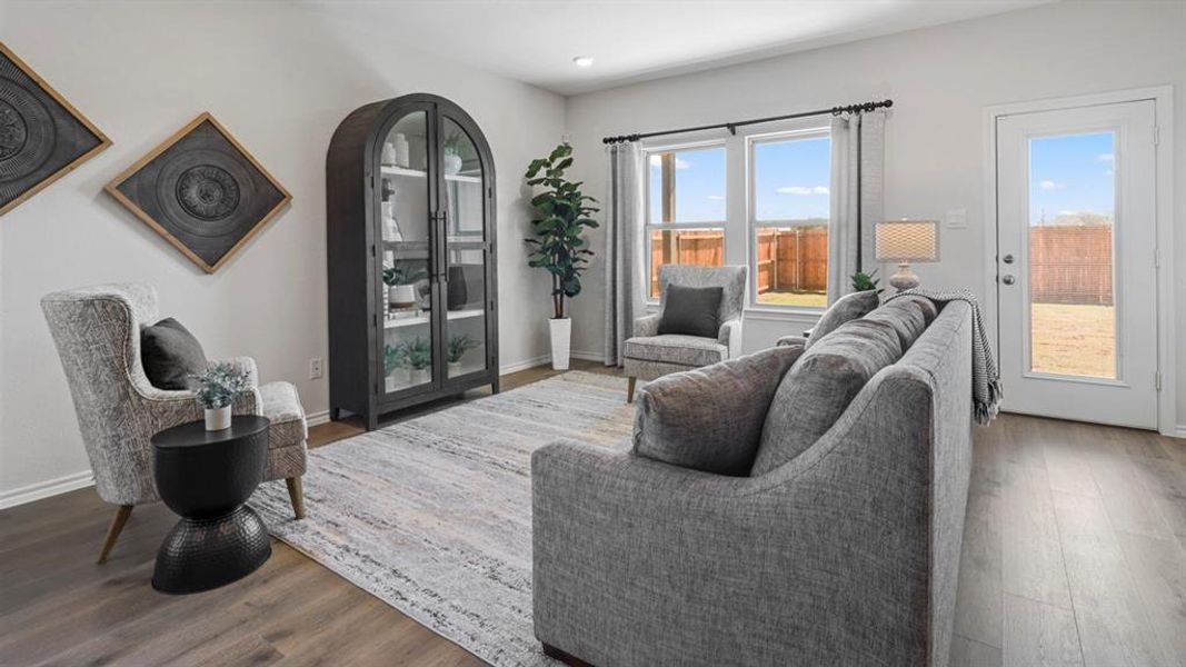 Spacious living area featuring wood-finish flooring, light grey walls, white trim, and multiple windows providing ample natural light
