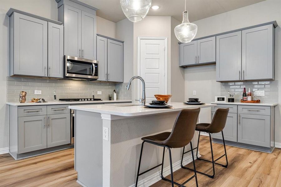 Kitchen with an island with sink, light wood-type flooring, backsplash, and sink